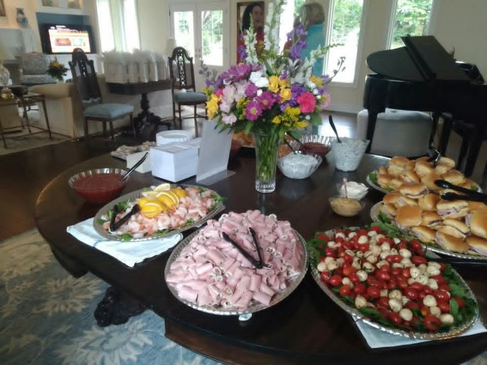 Catering spread with sandwiches, caprese salad, sliced meats, shrimp, and dips