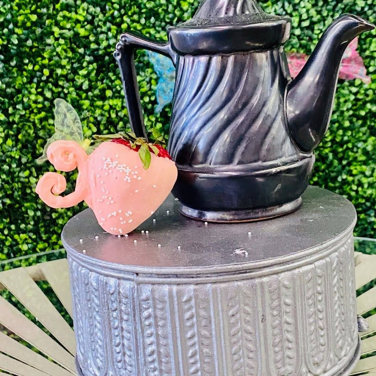 Decorative teapot display with a pink chocolate-covered strawberry