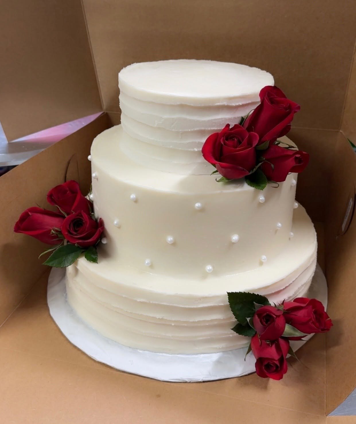 Three-tier white wedding cake with red roses